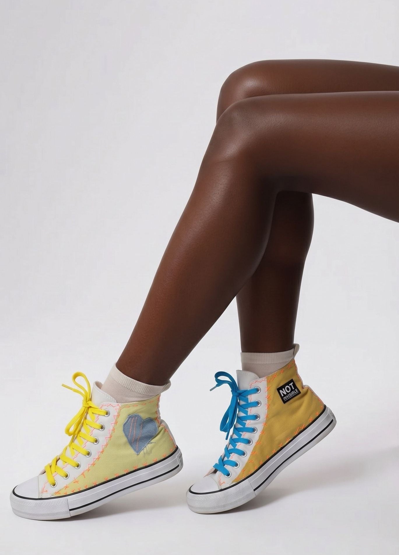 Yellow high-top sneakers with blue laces worn by a person on a white background